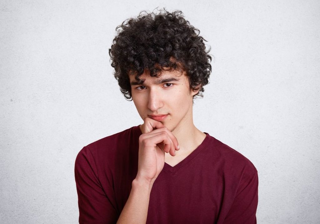 Man with a short curly crop, 1.5 inches of curls on top and sides blended up from a #2 guard